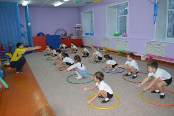 Инструктор по физкультуре показывает детям упражнение в обруче