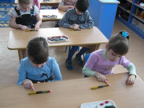 Дети в пара за столами складывают в ряд разноцветные палочки палочки Кюизенера