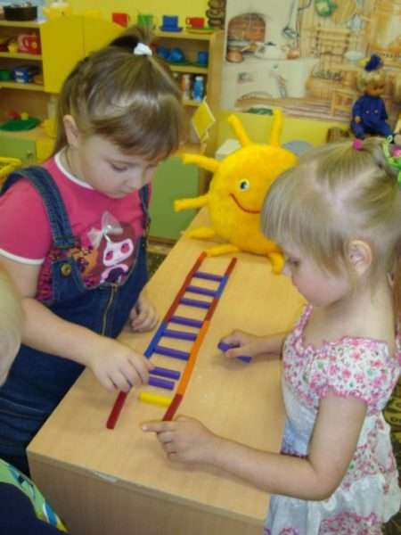 Две девочки строят лесенку из палочек к солнышку