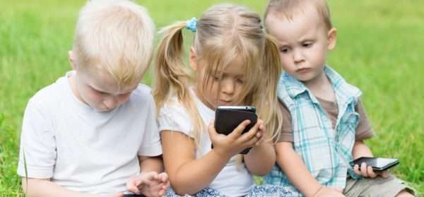 Дети дошкольного возраста сидят с мобильными телефонами и смотрят в экраны