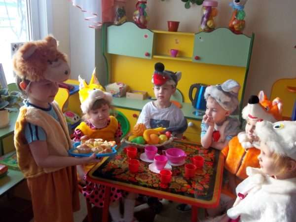 Дети в костюмах животных сидят за столом с игрушечной посудой и фруктами