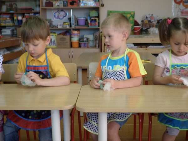 Дети сидят за столами в фартуках и держат в руках пакетики с песком