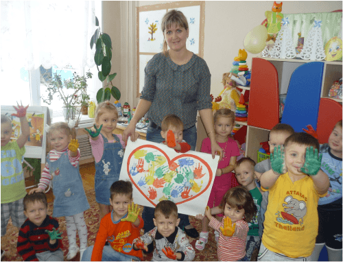 Дети и воспитательница держат проект Сердце из ладошек