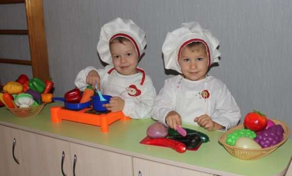 Две девочки в костюмах поваров играют в кухню