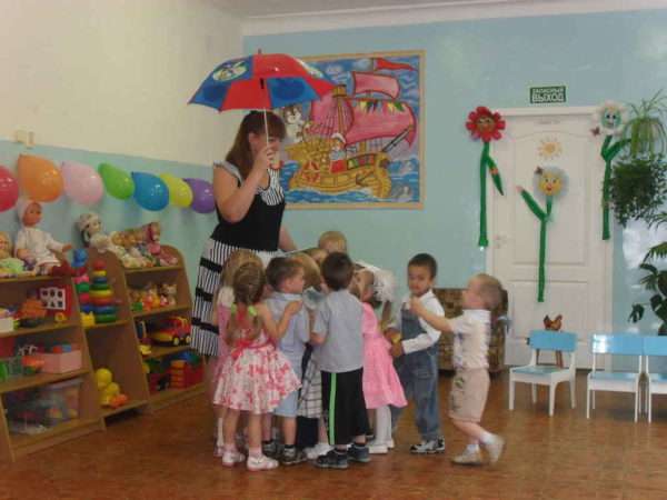 Воспитатель держит в руке яркий зонт, дети стоят рядом