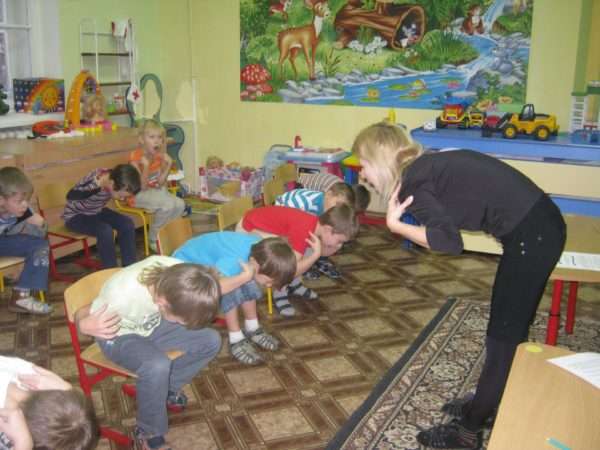 Дети делают физкультминутку на стульчиках, педагог показывает движения