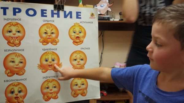 Мальчик показывает своё настроение на плакате с изображениями различных эмоций