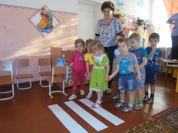 Дети и педагог стоят перед импровизированным пешеходным переходом в помещении группы