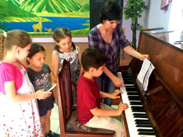 Мальчик сидит за фортепиано, воспитатель и трое детей стоят рядом