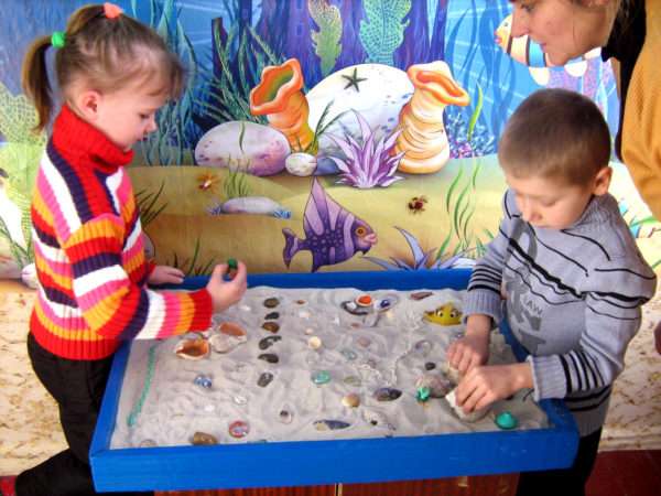 Мальчик и девочка играют в песочнице с ракушками и другими мелкими предметами