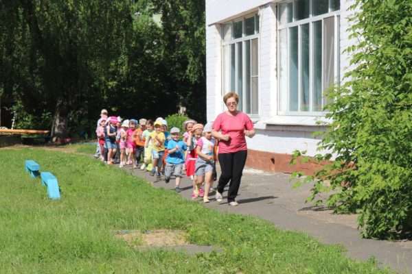 Дети идут спортивной ходьбой по территории детского сада