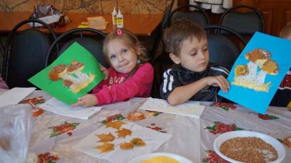 Девочка и мальчик сидят за столом и показывают аппликации с грибами