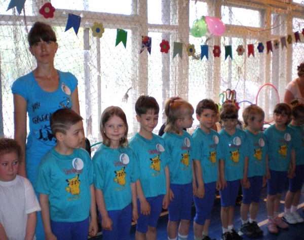 Дети, воспитательница в синих футболках стоят на занятии физкультурой