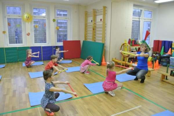 Дети выполняют упражнения с палкой рядом с ковриками для йоги