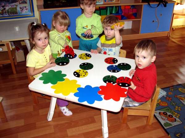 Дети сидят за столом, на котором разложены наглядные материалы разных цветов