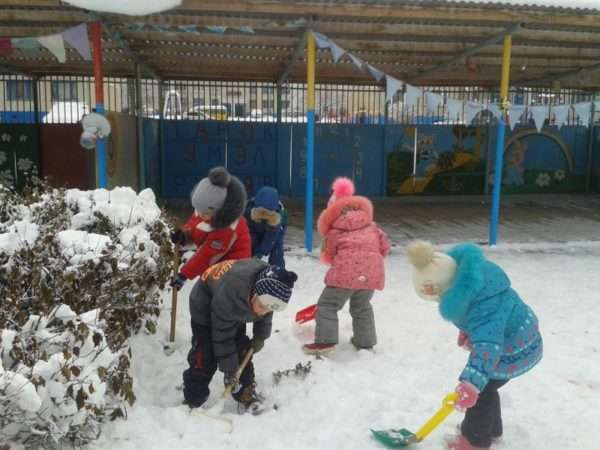 Дети сгребают лопатками снег на участке