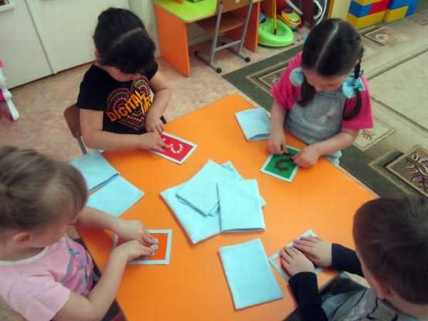 Дети сидят за столом, перед ними карточки с цифрами и листы картона