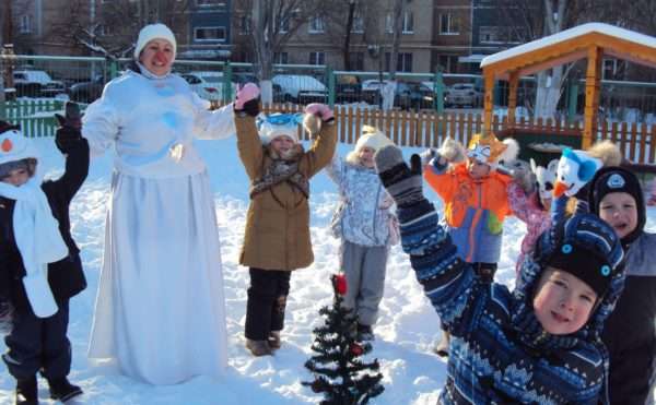 Дети и воспитатель в костюме снежной бабы на прогулке поднимают руки вверх