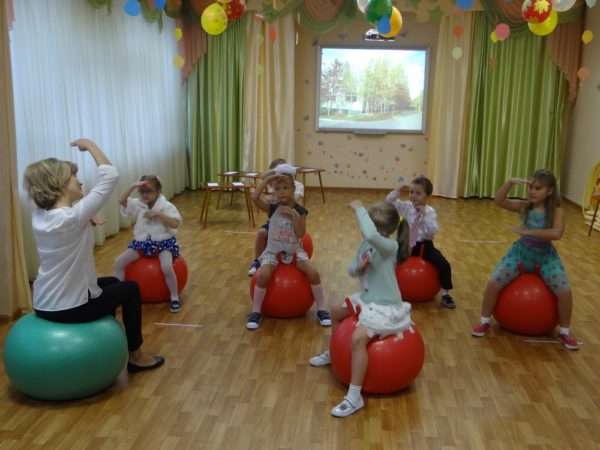Дети и педагог сидят на гимнастических шарах
