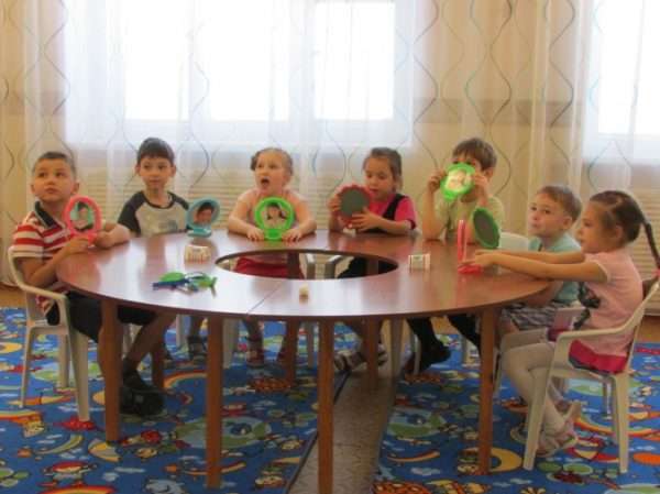 Дети сидят за круглым столом, держат в руках зеркала