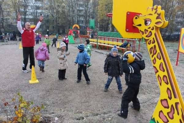 Инструктор по физкультуре и дети на спортивной площадке играют с мячом