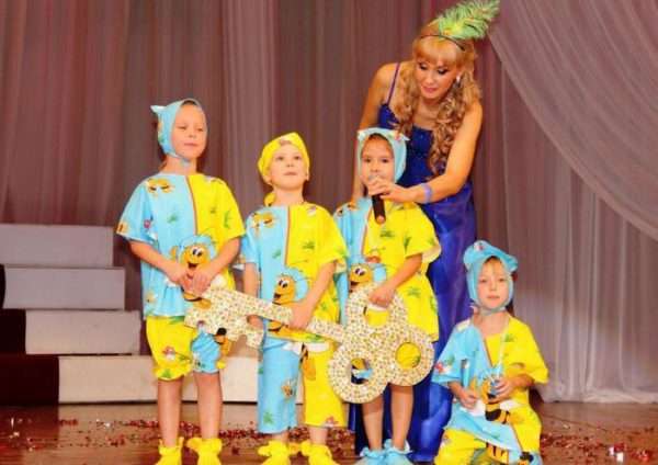 Воспитательница и четыре ребёнка в костюмах на сцене, дети держат большой ключ