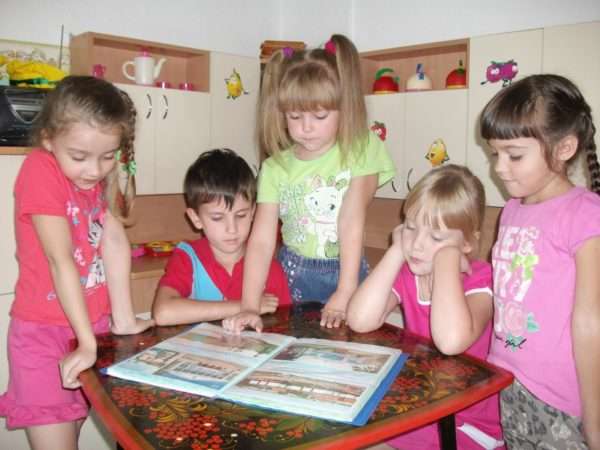 Четыре девочки и мальчик рассматривают иллюстрации в книге