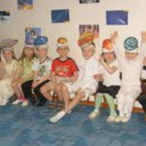Дети с шапочками в виде небесных тел сидят на стульчиках