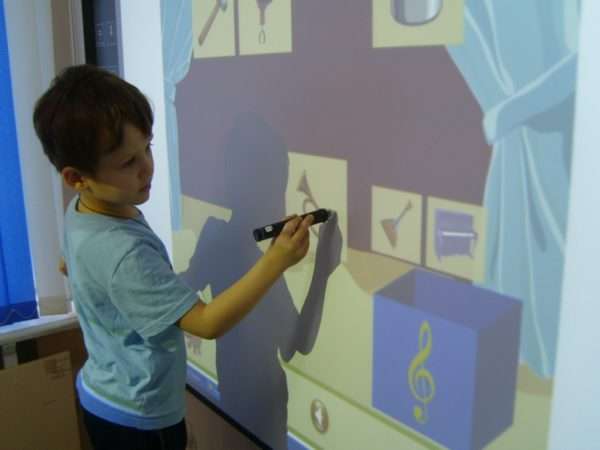 Мальчик выполняет задание на интерактивной доске с изображениями музыкальных инструментов