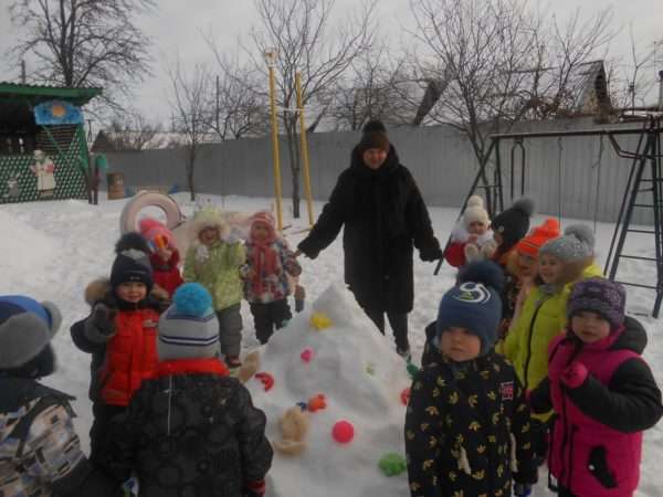 Дети и воспитательница стоят вокруг кучи снега