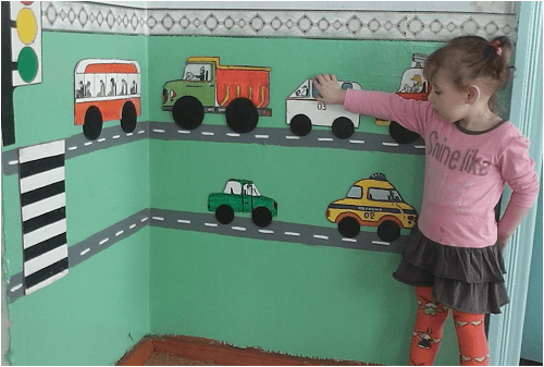Девочка рассматривает бумажные модели разных видов машин