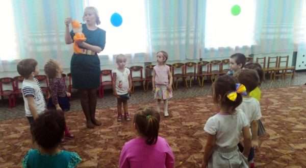 Воспитатель рассказывает что-то детям, стоящим в кругу, от лица игрушки